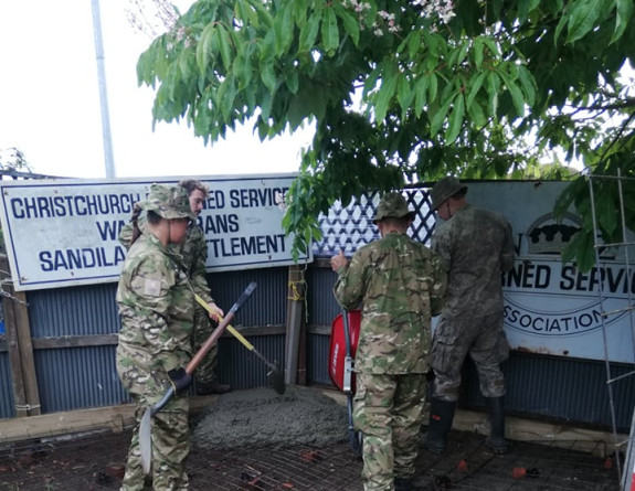 Four Army Reserves pour concrete into an area outside under a tree. 