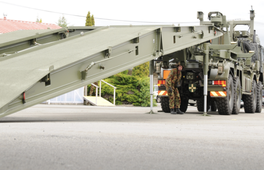 A soldier supervises as another deploys the Rapidly Emplaced Bridge System (REBS) on tarmac.