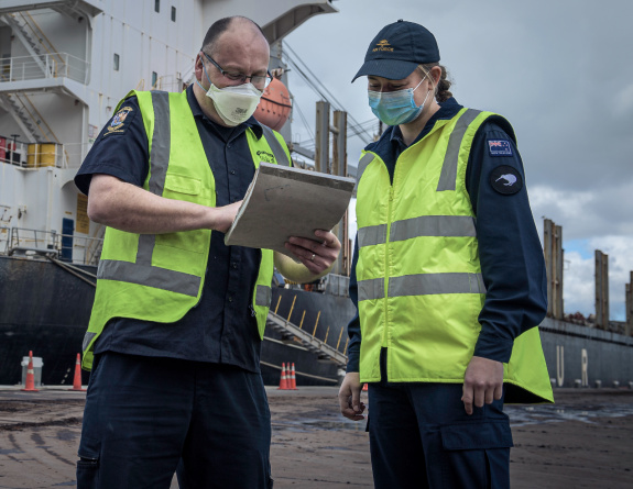 NZDF personnel wearing high vis and masks discuss matters of a clipboard at the border in support of the All of Government COVID-19 response