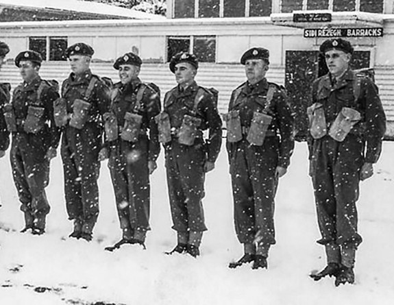 The image is black and white. Soldiers stand at attention in the snow. This image is taken from 1955