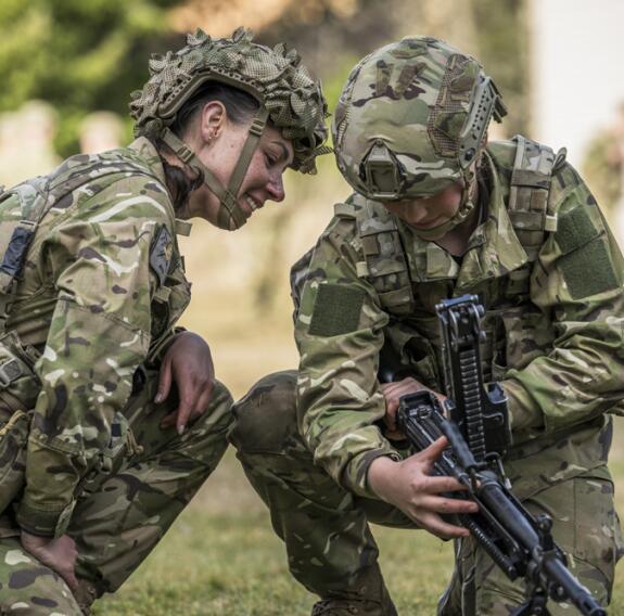Two soldiers look inside the barrel of a weapon.