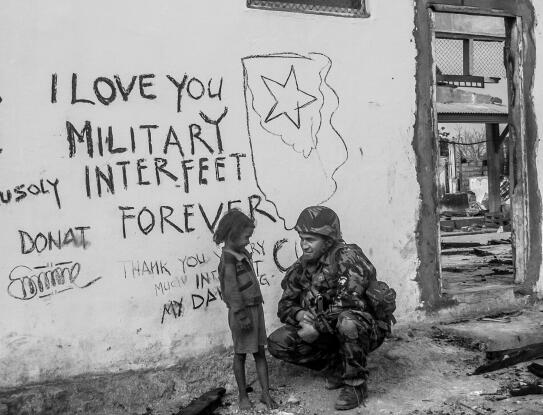Little girl talking with soldier on street with graffiti.