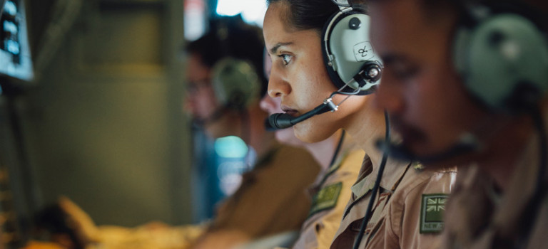 Three Air Force personnel wearing headsets and looking at screens on board a P3K-2 Orion