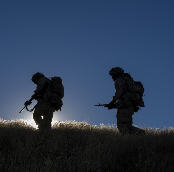 Three New Zealand Army soldiers silhouetted on the top of hill - one backlit from the sun. 