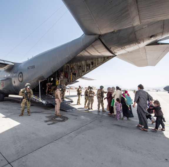Evacuees board a Royal New Zealand Air Force C-130H(NZ) Hercules aircraft at Hamid Karzai International Airport in Kabul. NZDF personnel stand at the ramp of the aircraft to support them and provide security