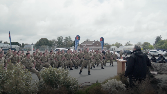 Soldiers in full uniform are pictured mid-haka, knees bent, hands on chest and mouths open.